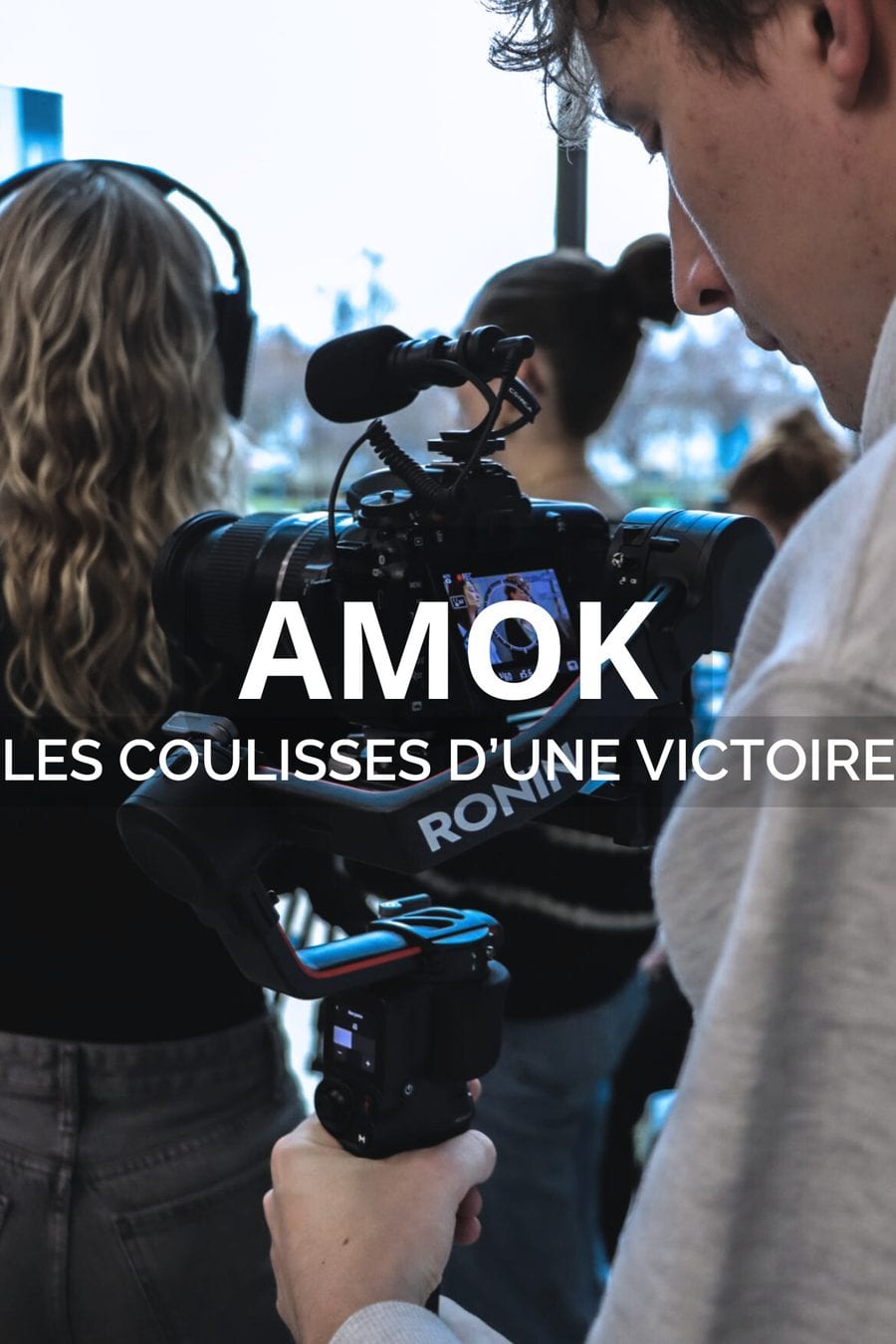 Un cadreur filme à l’épaule avec une caméra sur stabilisateur et micro canon, entouré de l’équipe en extérieur. Titre incrusté : AMOK, les coulisses d’une victoire.